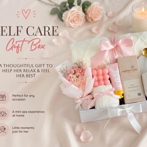 May include: A white gift box filled with self-care items, including a pink bow-tied blanket, a bouquet of flowers, a pink soap, a tube of rose-scented cream, and a chocolate bar. The box is tied with a white ribbon and is surrounded by rose petals.