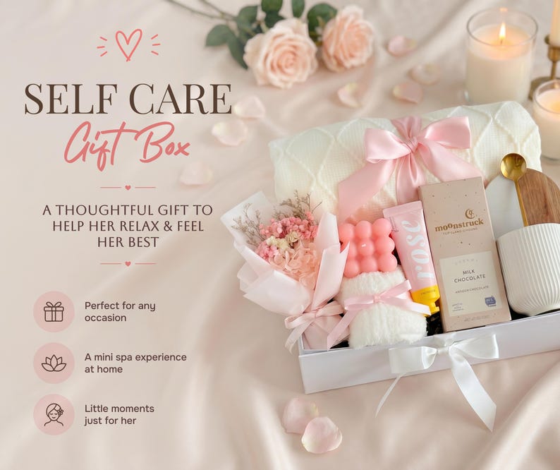 May include: A white gift box filled with self-care items, including a pink bow-tied blanket, a bouquet of flowers, a pink soap, a tube of rose-scented cream, and a chocolate bar. The box is tied with a white ribbon and is surrounded by rose petals.