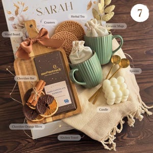 May include: A gift set containing a wooden board with a brown ribbon, a Moonstruck dark chocolate espresso bar, chocolate orange slices, cinnamon sticks, two ribbed green ceramic mugs with cloth bags, two gold spoons, a bubble candle, and a kitchen towel.
