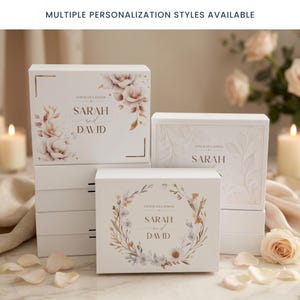 May include: White gift boxes with floral and botanical designs. The boxes feature the names "Sarah and David" and the word "Congratulations". The boxes are decorated with watercolor flowers and leaves. The text "MULTIPLE PERSONALIZATION STYLES AVAILABLE" is at the top.