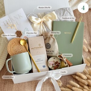 May include: A white gift box filled with a variety of items, including a blanket, a notebook and pen, a mug, a chocolate bar, herbal tea, a candle, and cinnamon sticks. The box is tied with a white ribbon and has the number 4 on the top.