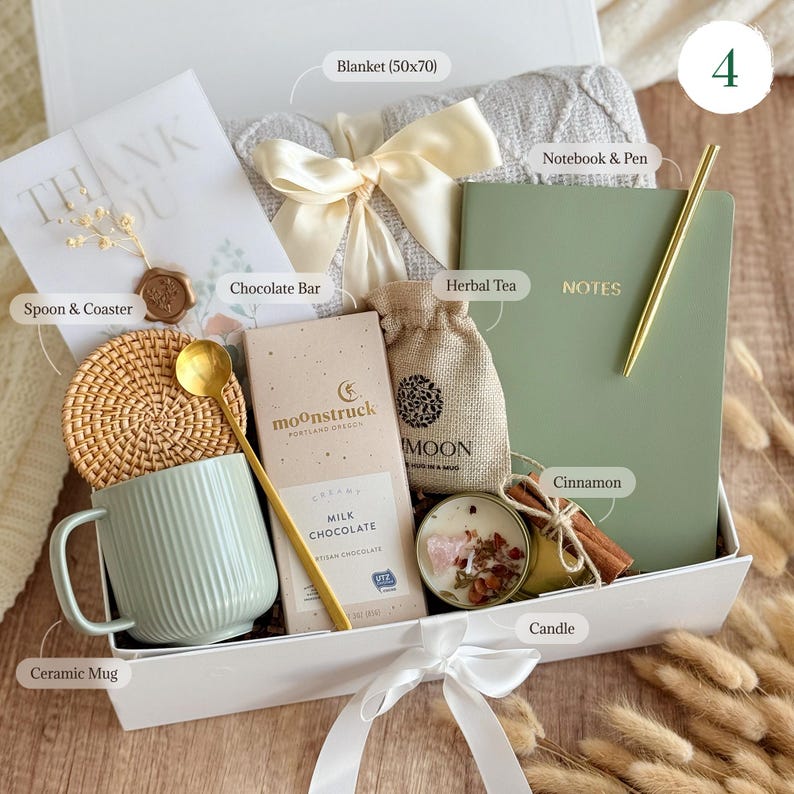 May include: A white gift box filled with a variety of items, including a blanket, a notebook and pen, a mug, a chocolate bar, herbal tea, a candle, and cinnamon sticks. The box is tied with a white ribbon and has the number 4 on the top.