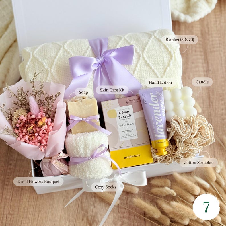 May include: A white gift box filled with self-care items. Includes a cream-colored blanket (50x70 inches), lavender-scented hand lotion, a candle, a skin care kit, soap, a dried flower bouquet, cozy socks, and a cotton scrubber. A perfect gift.