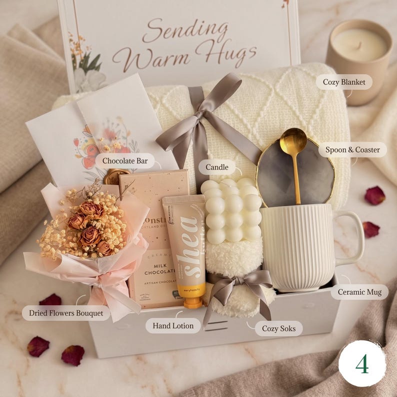 May include: A gift basket with a cozy theme, featuring a cream-colored blanket, a ceramic mug, a candle, and a bouquet of dried flowers. The basket also includes a chocolate bar, hand lotion, and cozy socks, all tied together with a ribbon.