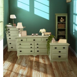 May include: A bedroom scene featuring light green furniture, including a dresser, nightstand, and tall chest. The room has a teal wall, hardwood floors, and is decorated with lamps, books, and framed artwork. Sunlight streams through a window.