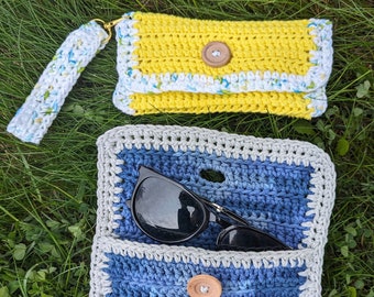 May include: Two crocheted bags, one yellow with white trim and one blue with gray trim. Both bags have a button closure and are made with a textured stitch. The blue bag has a pair of sunglasses inside.