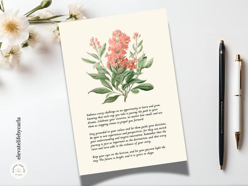 May include: A rectangular card with a cream background featuring a botanical illustration of pink flowers with green leaves at the top. Below the illustration, black text provides an inspirational message. The card is positioned next to two pens.