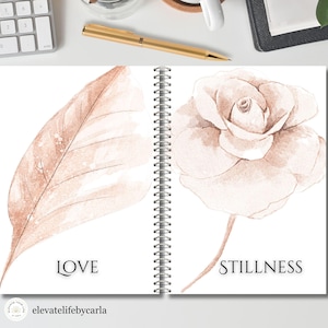 Può includere: Un taccuino a spirale aperto su due pagine con illustrazioni ad acquerello in tenui toni marroni. La pagina sinistra mostra una grande foglia con la parola LOVE stampata sotto. La pagina destra mostra una rosa con la parola STILLNESS sotto.