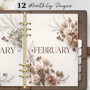 May include: A brown leather ring-bound planner open to pages labelled January and February. The pages feature cream-coloured paper with floral illustrations of roses, berries, and twigs. A gold-coloured metal binder mechanism holds the pages. The text 12 Monthly Pages is visible at the top, and a white and gold pen rests on the right side.