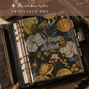 Op de afbeelding: Een planner-dashboard met een donkere achtergrond en een botanisch patroon van gele citrusslices, witte bloemen en groene bladeren. De tekst "Cozy Days Ahead" staat in het midden gedrukt. Het dashboard zit in een bruine ringband.