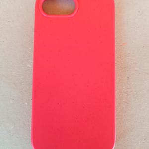 May include: A bright red phone case with a rectangular shape and a camera opening at the top. The case is made of a smooth material and is designed to protect a smartphone.