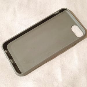 Peut inclure: Une coque de t&eacute;l&eacute;phone grise avec une finition mate. La coque a une forme rectangulaire avec des coins arrondis et un trou pour l'appareil photo. L'int&eacute;rieur est d'une nuance de gris plus claire. La coque est con&ccedil;ue pour prot&eacute;ger un t&eacute;l&eacute;phone.