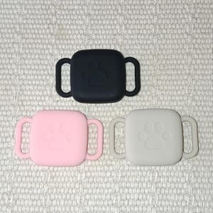 Può includere: Tre supporti in silicone per targhette per animali domestici in nero, rosa e bianco. Ogni supporto quadrato ha un design a zampa e due maniglie ad anello. I supporti sono progettati per contenere targhette per animali domestici.