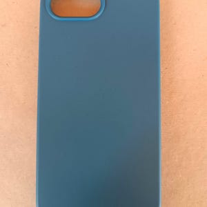 May include: A teal-colored phone case with a rectangular shape and rounded corners. The case has an oval opening for the camera lens. The smooth, solid-colored case is designed to protect a mobile phone.