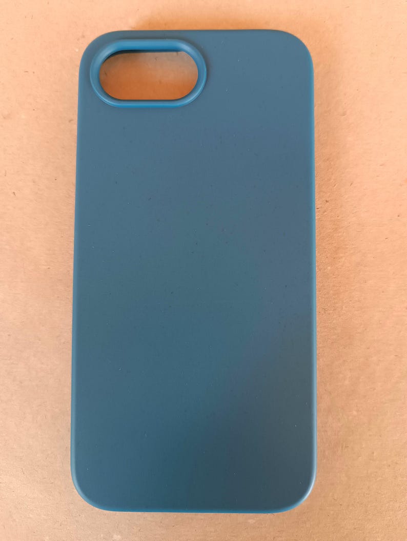 May include: A teal-colored phone case with a rectangular shape and rounded corners. The case has an oval opening for the camera lens. The smooth, solid-colored case is designed to protect a mobile phone.