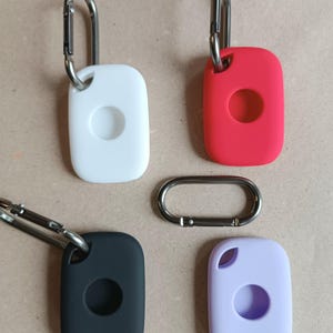 May include: Four silicone key covers with a metal carabiner clip. The covers are in white, red, black, and purple.