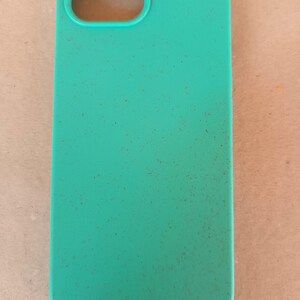 May include: A teal phone case with a rectangular shape and rounded corners. The case has an oval cutout for the camera and a speckled texture. The case is designed to protect a smartphone.