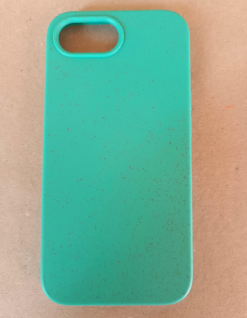 May include: A teal phone case with a rectangular shape and rounded corners. The case has an oval cutout for the camera and a speckled texture. The case is designed to protect a smartphone.