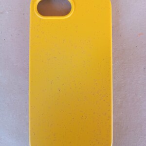 May include: A bright yellow phone case with a speckled texture. The case has a rectangular shape with rounded corners and a camera opening at the top. The case is designed to protect a smartphone.