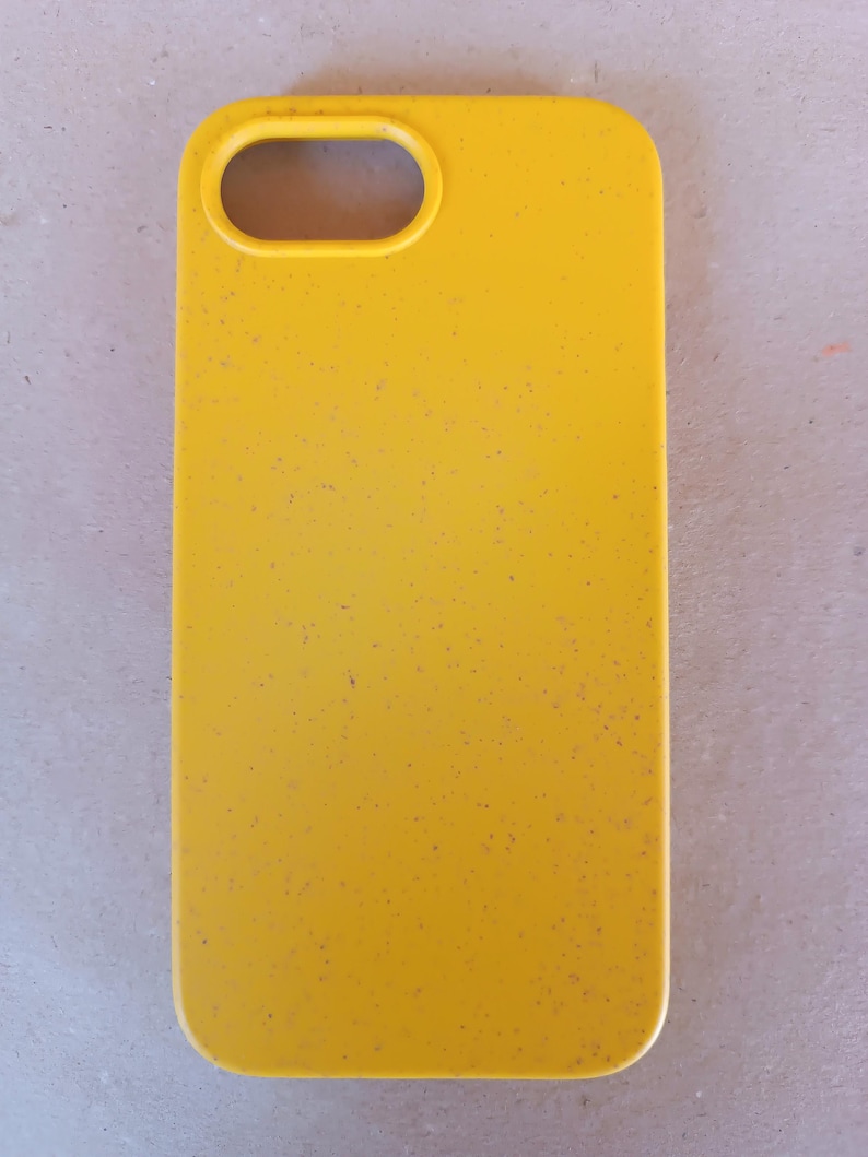 May include: A bright yellow phone case with a speckled texture. The case has a rectangular shape with rounded corners and a camera opening at the top. The case is designed to protect a smartphone.