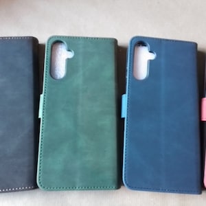 Könnte beinhalten: Vier Handyhüllen in verschiedenen Farben: Schwarz, Grün, Blau und Rot. Die Hüllen sind aus Leder und haben eine Klappe, die den Bildschirm bedeckt.