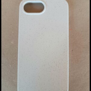 May include: A light beige phone case with a speckled texture. The case has a rectangular shape with rounded corners and a cutout for the camera lens. The case is designed to protect a phone.