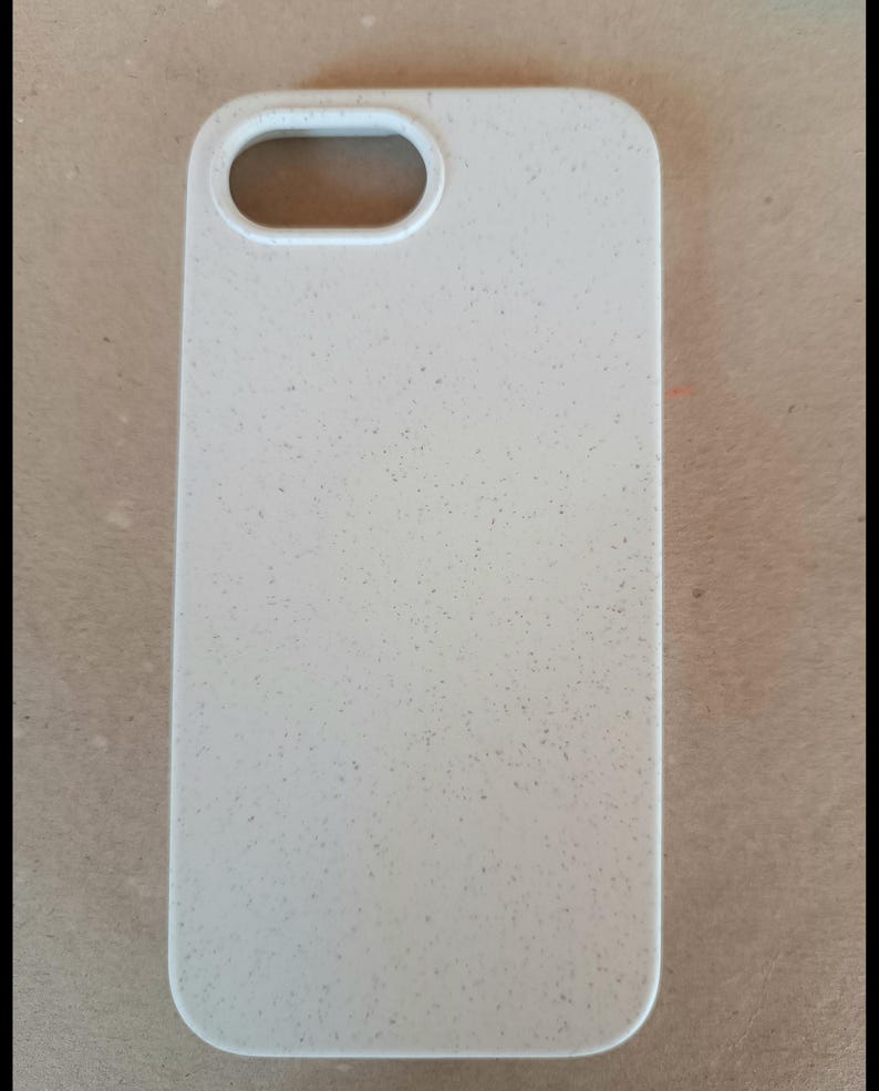 May include: A light beige phone case with a speckled texture. The case has a rectangular shape with rounded corners and a cutout for the camera lens. The case is designed to protect a phone.