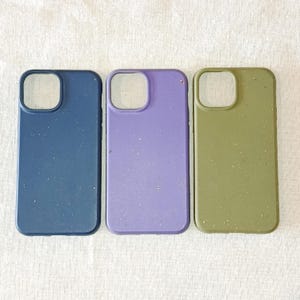 Op de afbeelding: Drie telefoonhoesjes op een rij, elk met een uitsparing voor de camera. De hoesjes zijn in tinten blauw, paars en olijfgroen. De hoesjes hebben een gespikkelde textuur en zijn gemaakt van een mat materiaal.