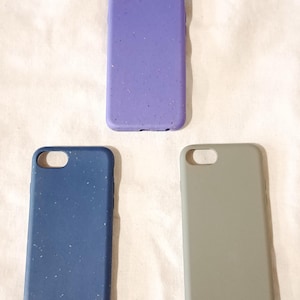 May include: Three phone cases in shades of purple, blue, and grey. The cases have a speckled texture and are designed to fit a specific phone model. The cases are arranged on a white surface.