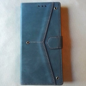 May include: A blue-gray phone case with a stitched design and a magnetic closure. The case has a geometric pattern with a flap and a button closure. The case has three small holes at the top and three metal eyelets.