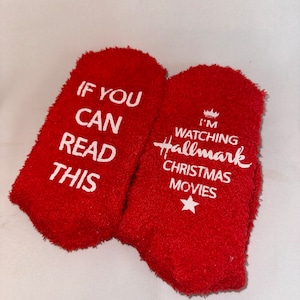 May include: A pair of red fuzzy socks with white text. One sock says "If you can read this" and the other sock says "I'm watching Hallmark Christmas movies".