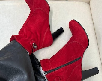 May include: A pair of red suede ankle boots with block heels. The boots have a zipper on the side and a buckle detail on the back.