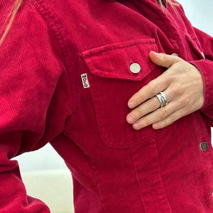 Puede incluir: Una chaqueta de pana roja con cierre de botones y un solo bolsillo en el pecho izquierdo. El bolsillo tiene una peque&ntilde;a etiqueta "MOTO".