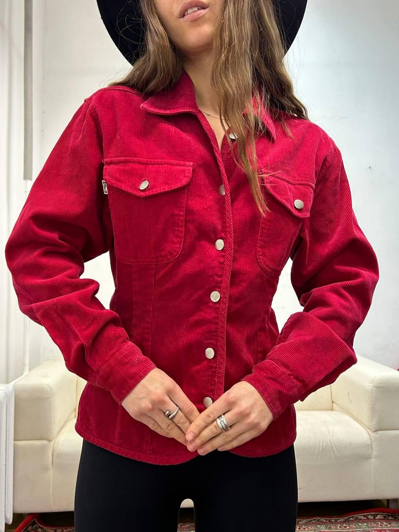 Puede incluir: Una camisa de pana roja con botones, mangas largas y silueta ajustada.
