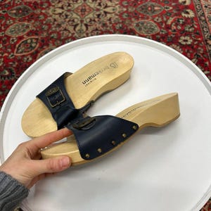 Könnte beinhalten: Paar blaue Ledersandalen mit Holzsohlen und einem Schnallenverschluss. Die Sandalen tragen den Markennamen "Birkenstock" auf der Sohle.