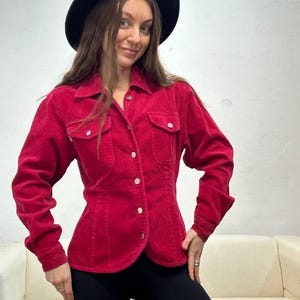 Puede incluir: Una camisa de pana roja con botones, mangas largas y cintura ajustada. La camisa tiene un cuello cl&aacute;sico y dos bolsillos de solapa en el pecho.