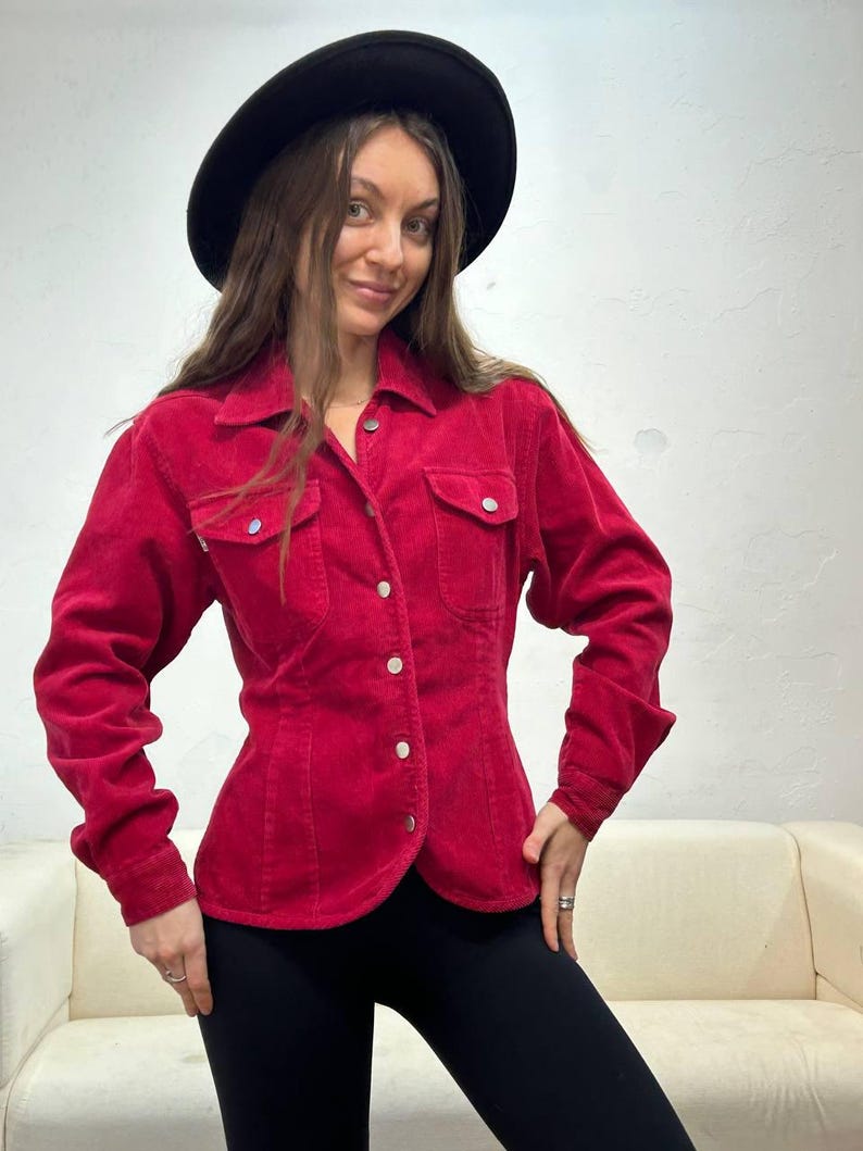 Puede incluir: Una camisa de pana roja con botones, mangas largas y cintura ajustada. La camisa tiene un cuello cl&aacute;sico y dos bolsillos de solapa en el pecho.