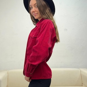 Puede incluir: Una camisa de pana roja con cuello y mangas largas. La camisa est&aacute; abotonada y tiene un corte holgado.