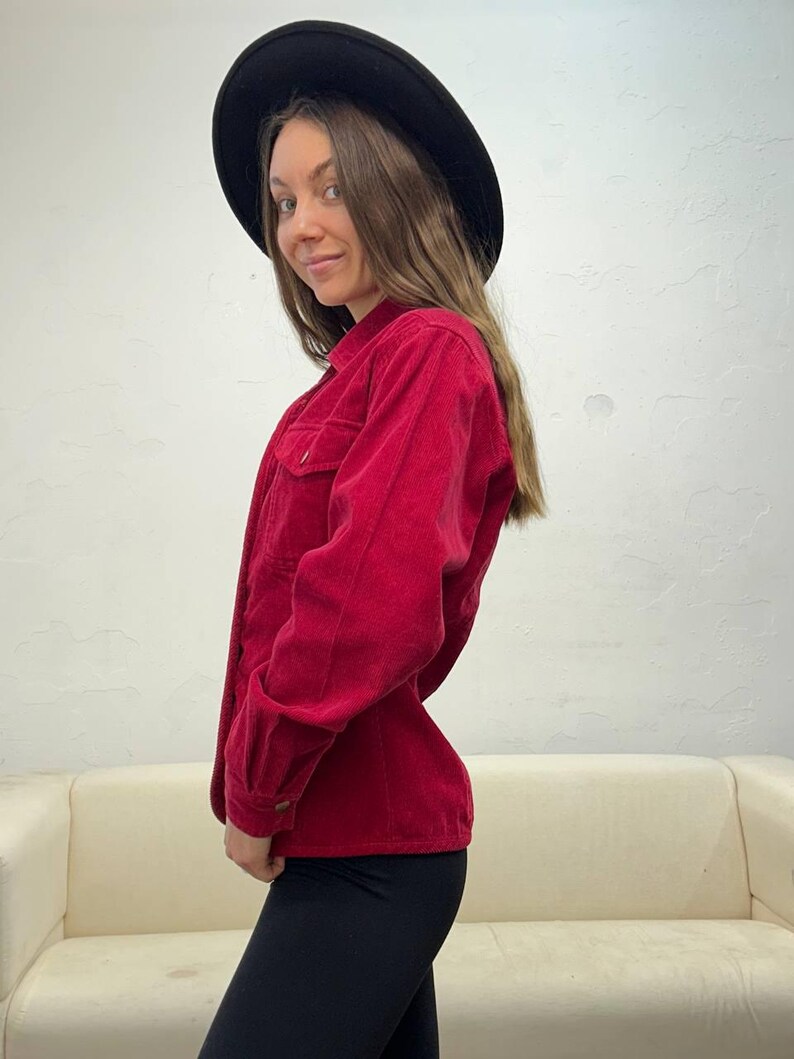 Puede incluir: Una camisa de pana roja con cuello y mangas largas. La camisa est&aacute; abotonada y tiene un corte holgado.