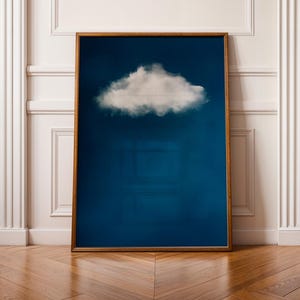 Puede incluir: Una impresión enmarcada de una sola nube blanca sobre un fondo azul oscuro. El marco es de madera marrón simple.