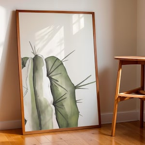 Puede incluir: Una pintura de acuarela enmarcada de un cactus verde con acentos blancos. El cactus se representa en un estilo minimalista con un fondo claro.