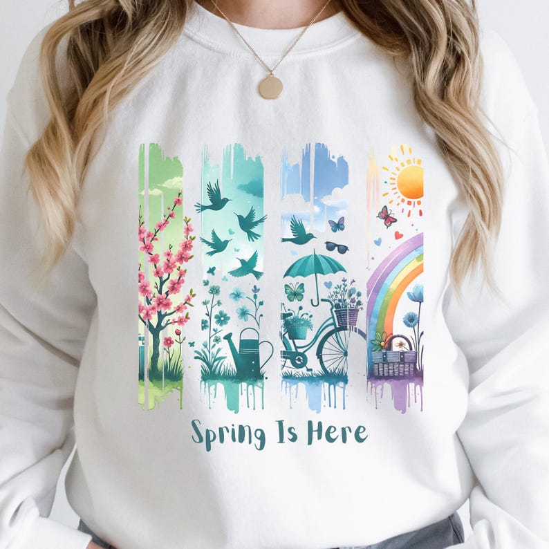May include: White sweatshirt with a colorful spring-themed graphic. The design features vertical panels with cherry blossoms, birds, flowers, a bicycle, and a rainbow. The words "Spring Is Here" are printed at the bottom of the graphic.