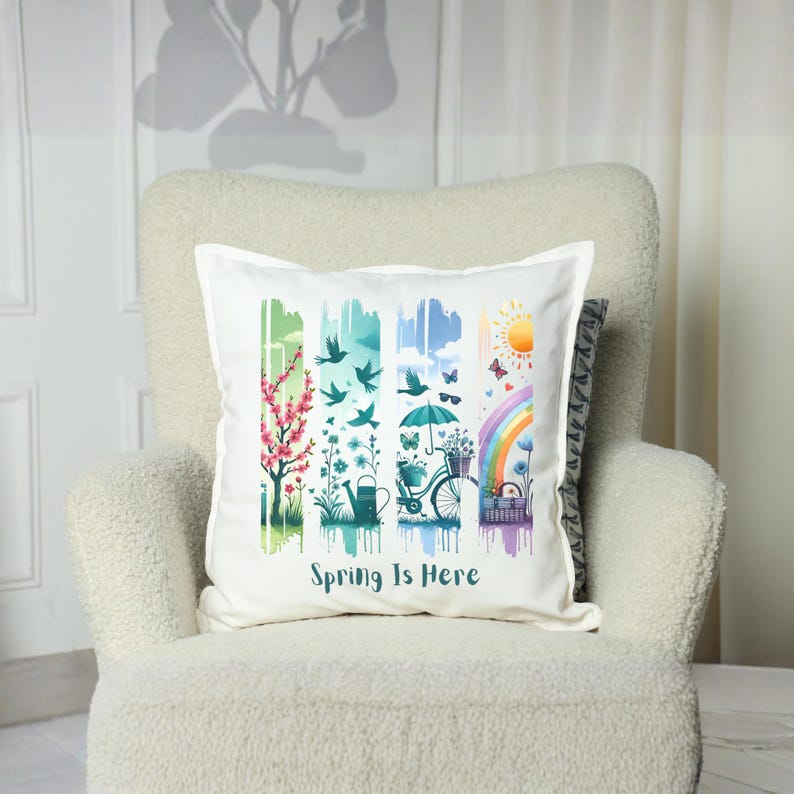May include: White square pillow with a colorful spring-themed design. The design includes images of a flowering tree, birds, a watering can, a bicycle with a basket of flowers, a rainbow, and a sun. The text "Spring Is Here" is printed on the pillow.