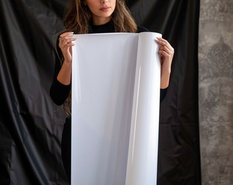 May include: A person holding a large, white, rolled-up sheet of paper. The paper is blank and the person is wearing a black shirt.