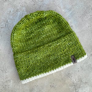 Pode incluir: Um gorro de malha verde com uma borda branca e uma etiqueta de couro marrom que diz "Hep".