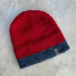 May include: Red and blue knitted beanie with a small brown label that says "Hep."