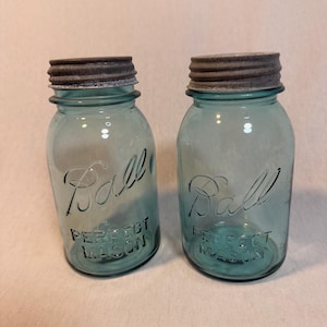 Op de afbeelding: Twee vintage blauwe Ball Perfect Mason potten met metalen deksels. De potten hebben reliëfletters en een klassiek ontwerp, perfect voor inmaken of decoratie. De potten zijn ongeveer 15 cm hoog.