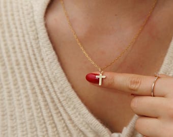 May include: A gold chain necklace with a small gold cross pendant. The necklace is worn by a person with red nail polish.