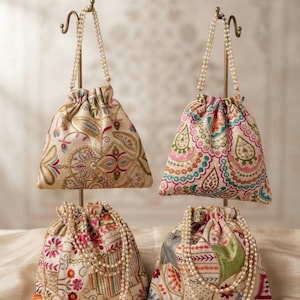 May include: Four drawstring pouches featuring intricate multi-colored embroidery on a cream-colored fabric base. Each pouch includes a delicate pearl bead handle and a gathered top closure, showcasing various floral and geometric patterns.