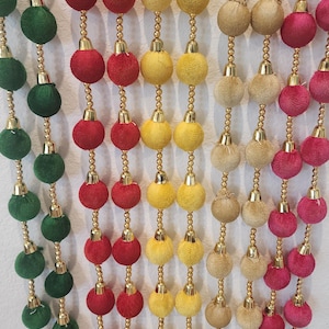 May include: A set of six decorative tassels with gold beads and colorful pom-poms. The tassels are made of fabric and have a fringe at the bottom. The colors of the pom-poms are green, red, yellow, beige, and pink.